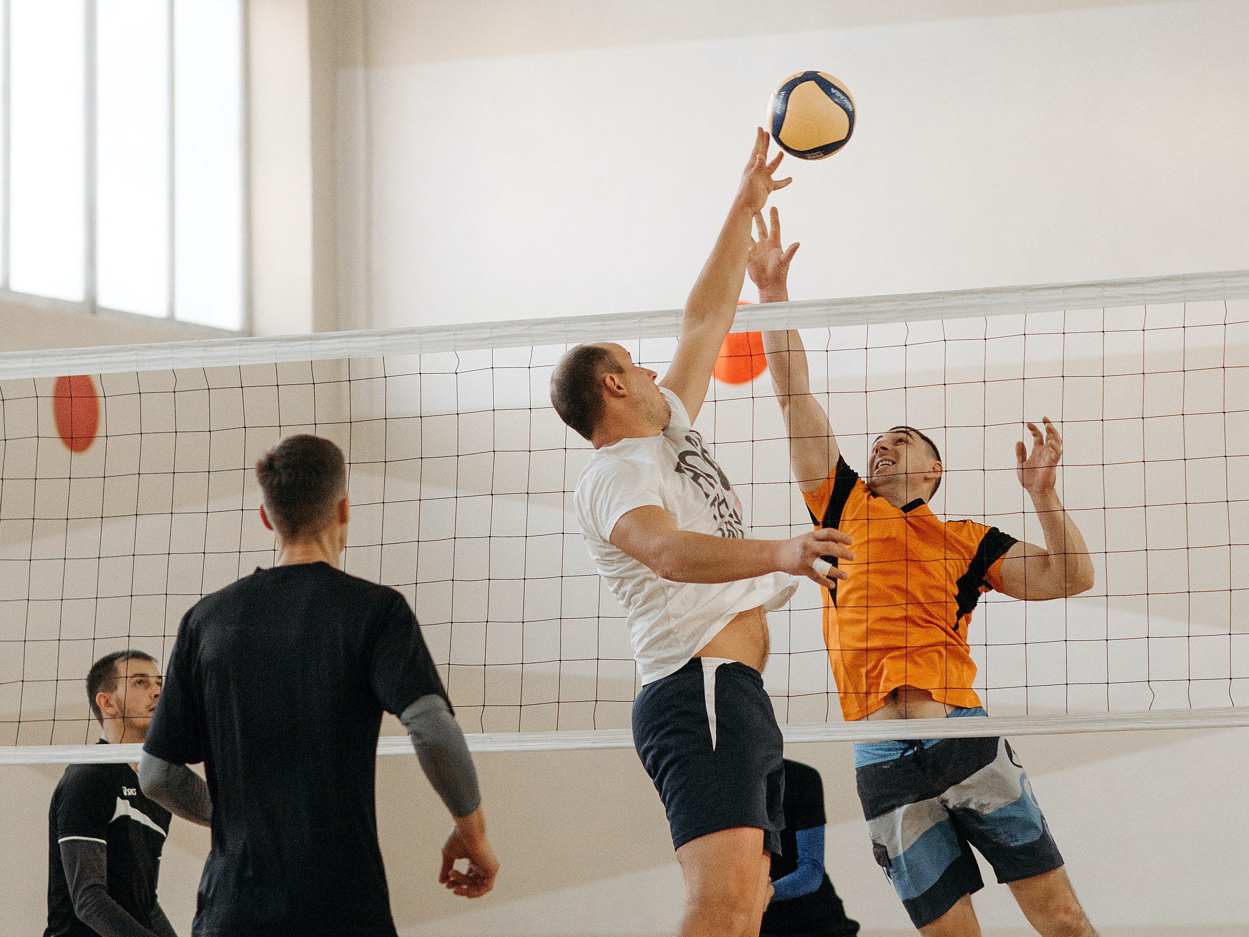 men playing volleyball. two of the men are jumping to attack the ball above the net.